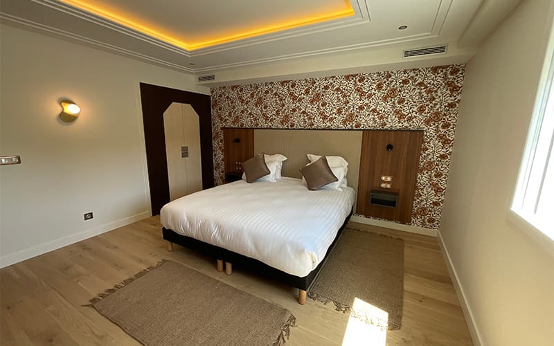 Chambre d’hôtel rénovée à Toulouse avec sol en bois, tête de lit sur mesure et éclairage LED encastré au plafond