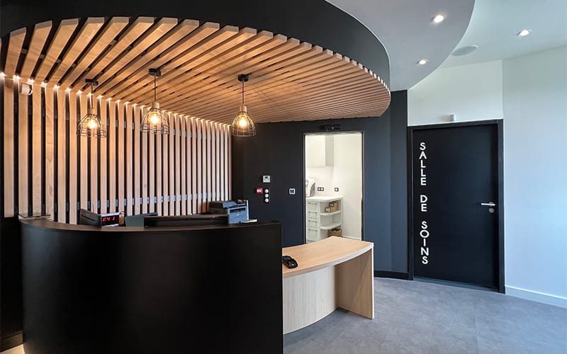 Accueil rénové d’un cabinet médical à Toulouse avec habillage bois, éclairage suspendu et design contemporain