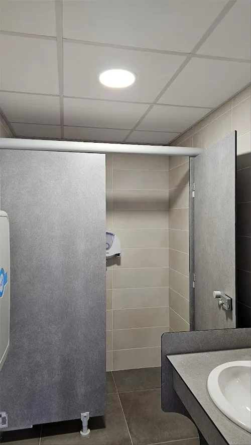 Cabine de sanitaires rénovée dans un hôtel à Toulouse, avec cloisons stratifiées, carrelage mural et éclairage LED conforme aux normes ERP.